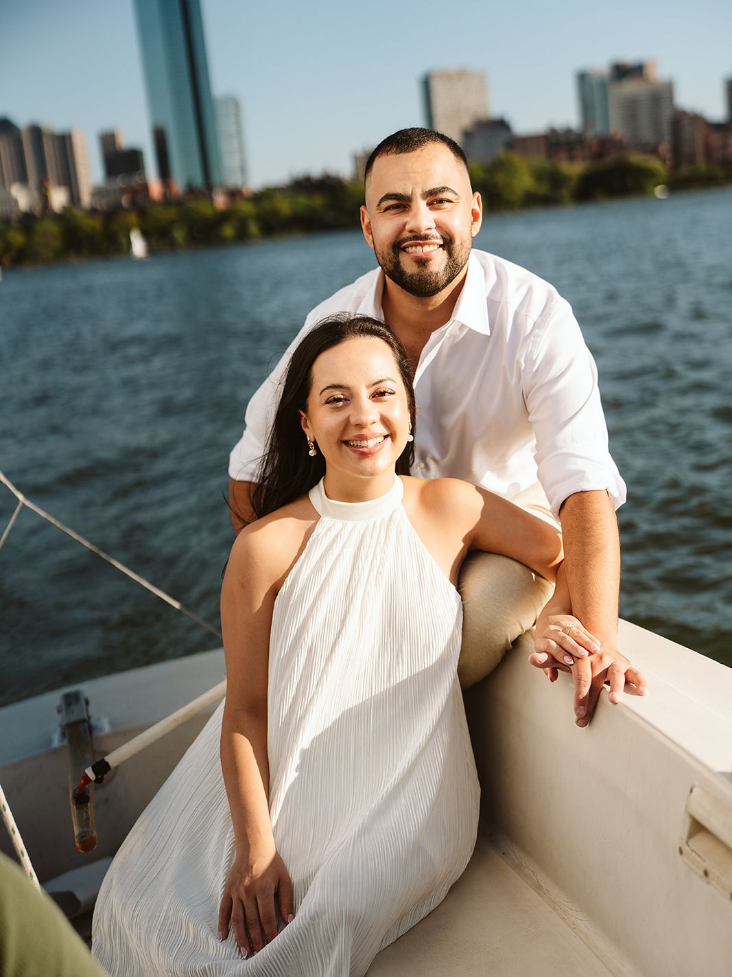 Doug and Julie smiling on a sailboat on the Charles River, the Boston skyline behind them